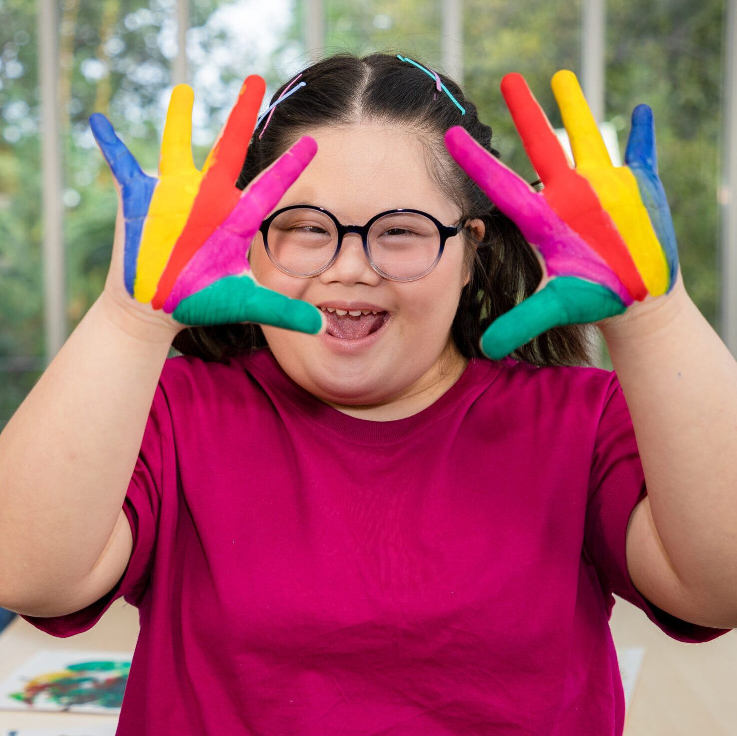young girl with down syndrome holding her hands up covered with paint