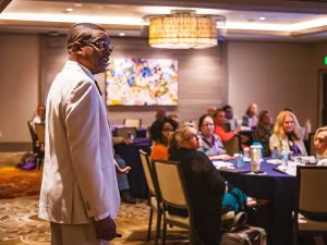 man speaking to crowd sitting at tables