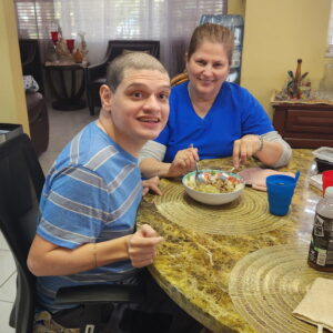 young man with disabilities sittting at table smling with caregiver
